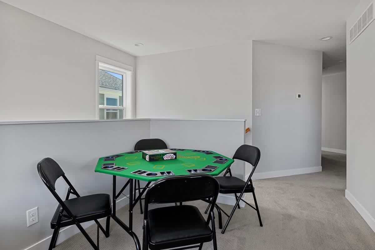 Loft area furnished with a green octagonal card table and four black folding chairs, ideal for games, set against light gray walls and carpeted flooring.
