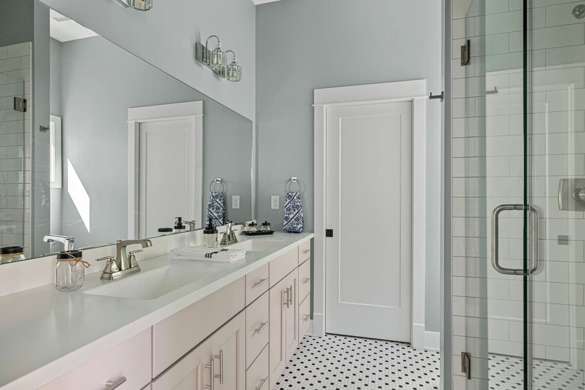 Modern bathroom with a double vanity featuring light-colored cabinets and white countertops, a large mirror, and a walk-in shower with white subway tiles and a glass door.