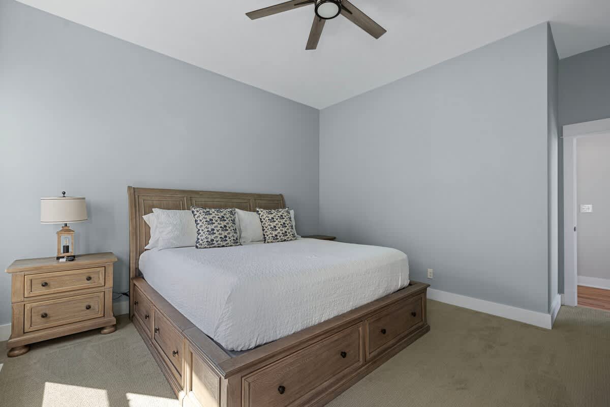 Spacious bedroom with light blue walls, a wooden king-sized bed with built-in storage, a matching nightstand with a lamp, and a ceiling fan.