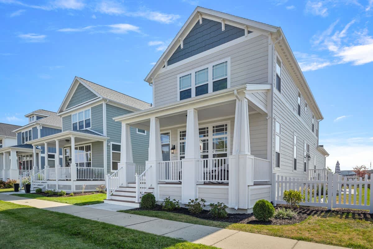 A charming two-story house with light gray siding and white trim, featuring a welcoming front porch with white columns and railings, and a well-maintained lawn.