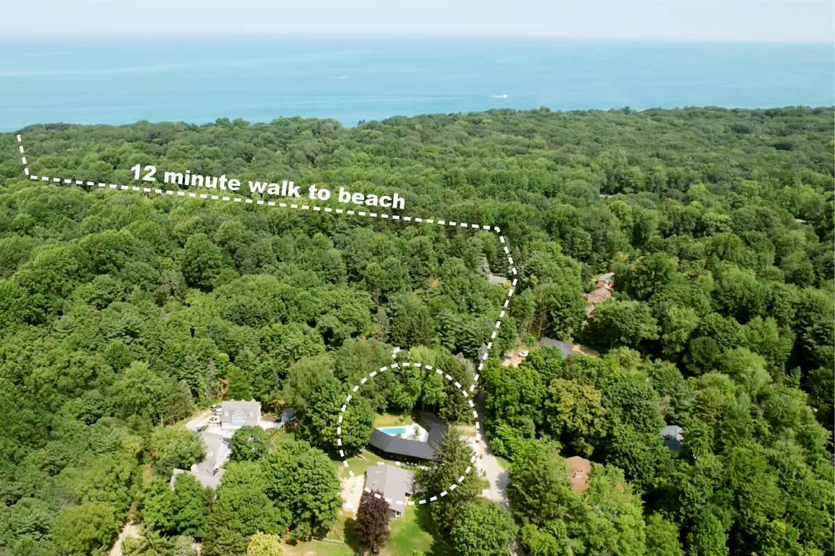 Aerial view of a lush green forested area, highlighting the property's location and a dotted line indicating a 12-minute walk to a large body of water, likely a beach or lake.