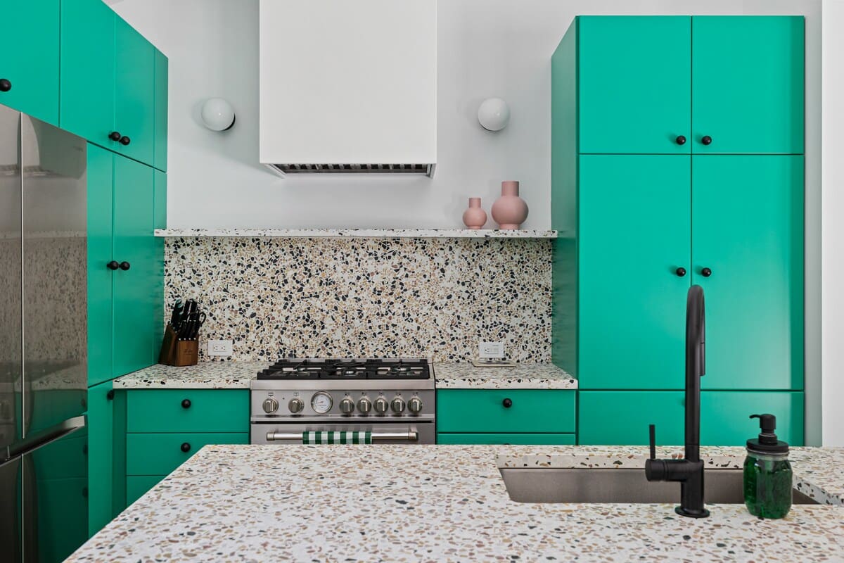 Detailed view of the kitchen's stainless steel range set against a speckled terrazzo backsplash and bright green cabinetry. A black faucet and sink are visible on the island.