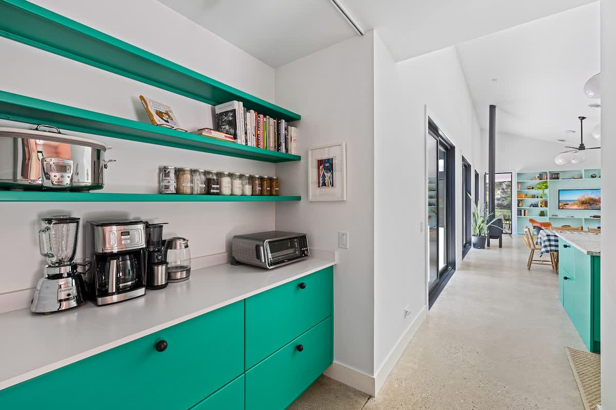 Functional pantry area with bright green open shelving stocked with kitchen items and a white countertop holding small appliances like a coffee maker and toaster.