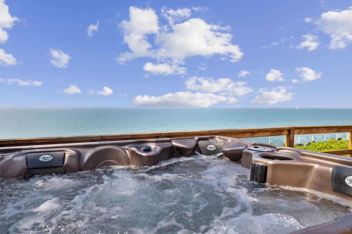 Close-up view of a bubbling hot tub on a wooden deck, with the vast expanse of a blue lake and a partly cloudy sky in the background.