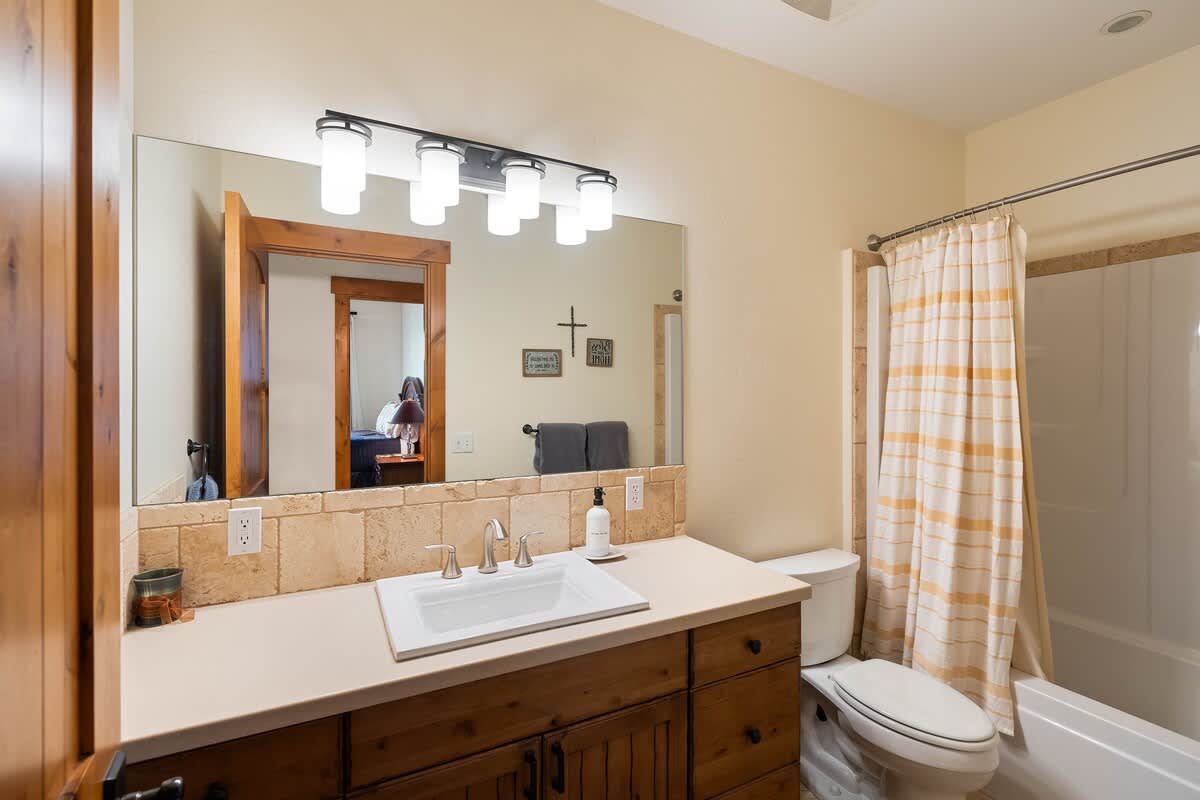 A functional bathroom with a wooden vanity, single sink, tiled countertop and backsplash, a toilet, and a shower/tub combo with a striped curtain.