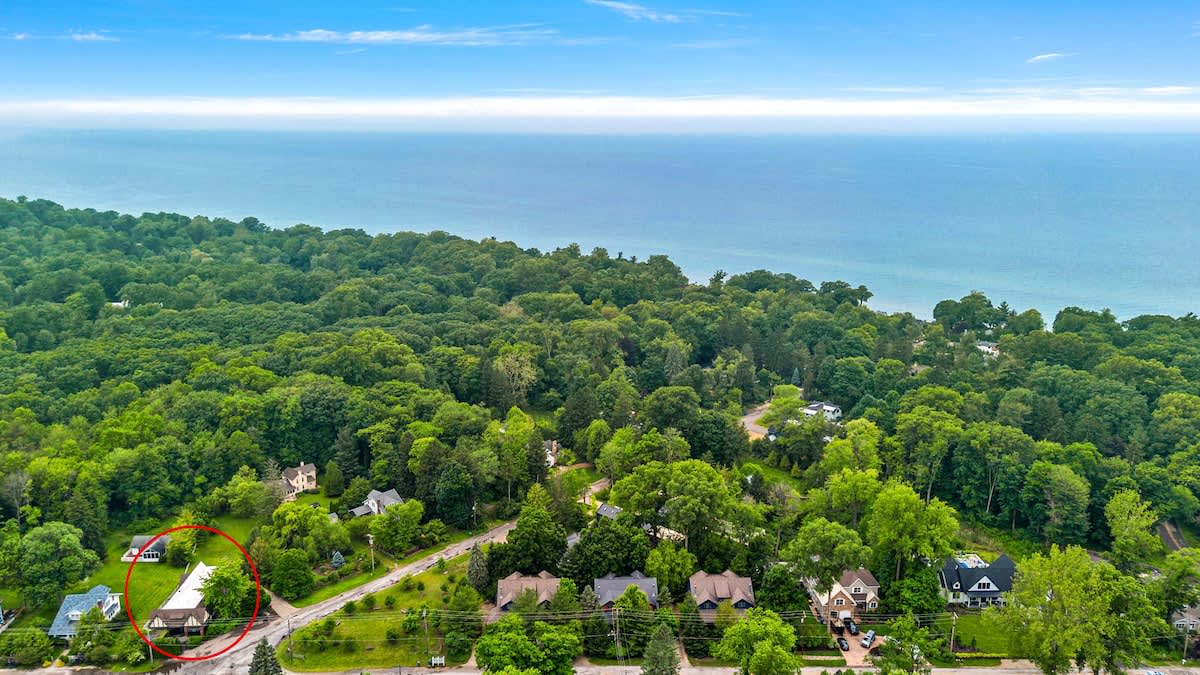 An aerial view highlights the property, circled in red, nestled among lush green trees, with the vast blue expanse of Lake Michigan visible in the background under a clear sky.