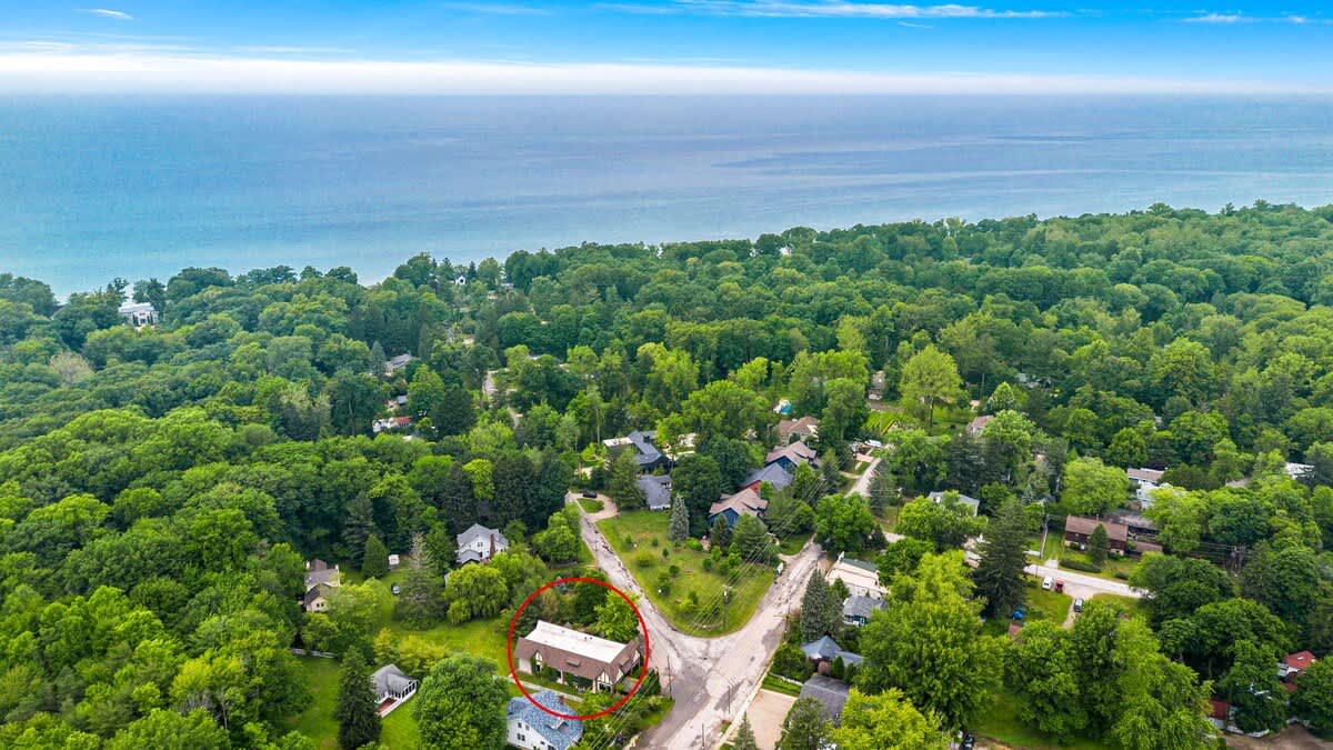 A wide aerial shot of the property, highlighted by a red circle, nestled within a dense green landscape, with a large body of water (Lake Michigan) visible in the distance.