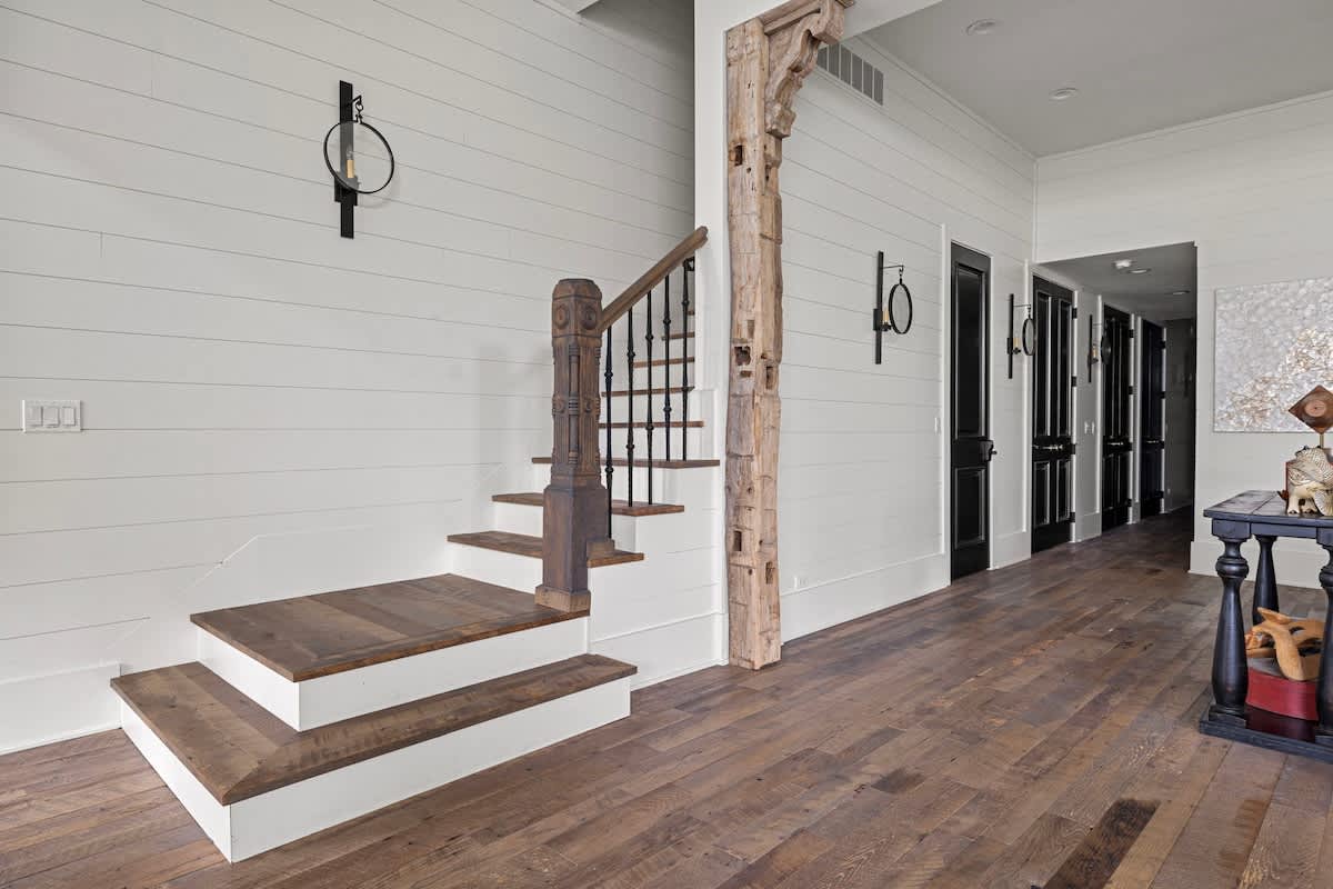 A welcoming foyer or hallway with a wooden staircase featuring wrought iron balusters, shiplap walls, and hardwood floors, leading to other rooms.
