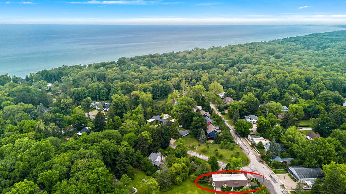 A high aerial perspective shows the property, circled in red, surrounded by a dense green canopy of trees, with the expansive blue waters of Lake Michigan stretching to the horizon.