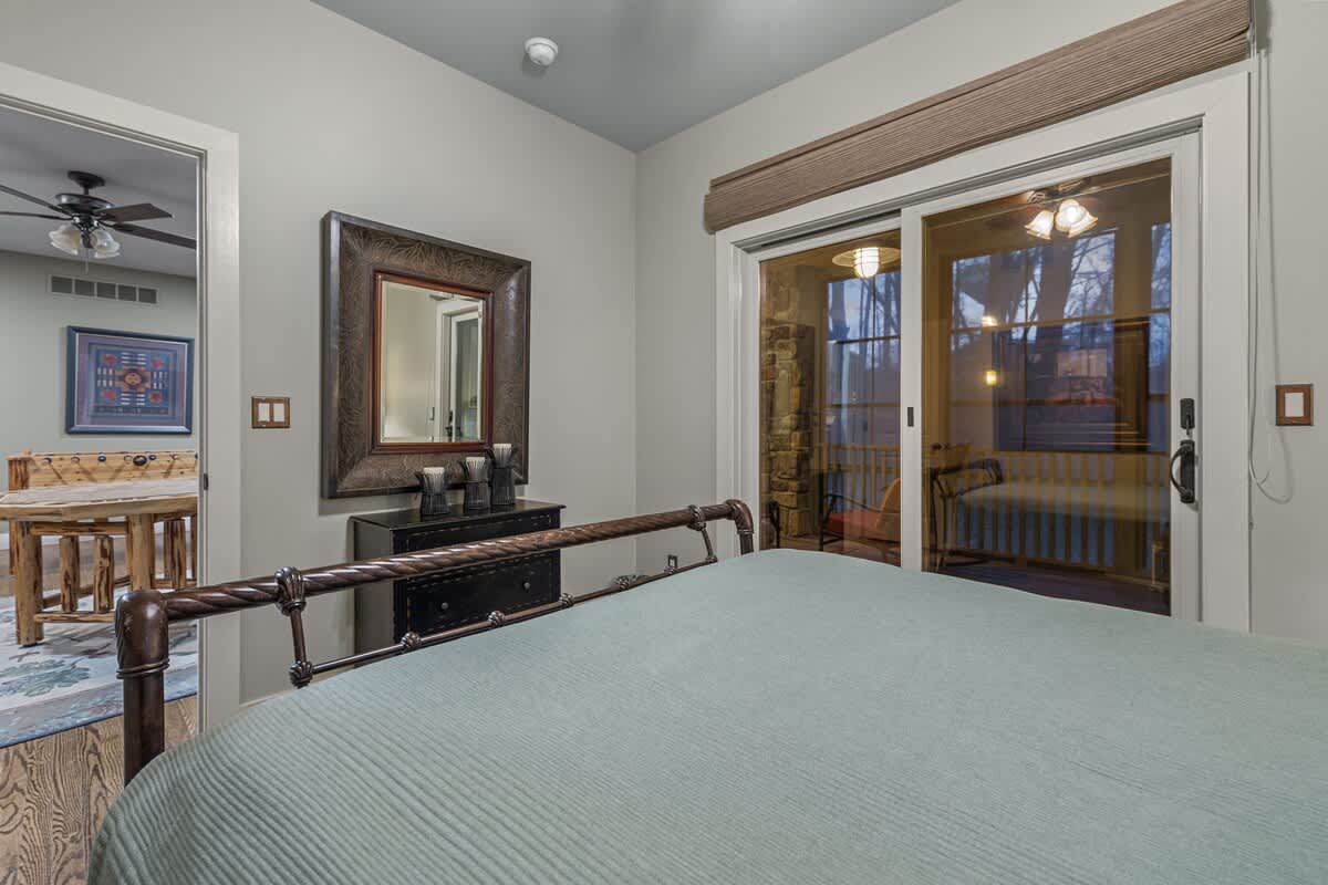 Serene bedroom with a wrought iron bed, hardwood floors, a dark dresser with a large framed mirror, and a sliding glass door to an outdoor screened porch, offering ample light.