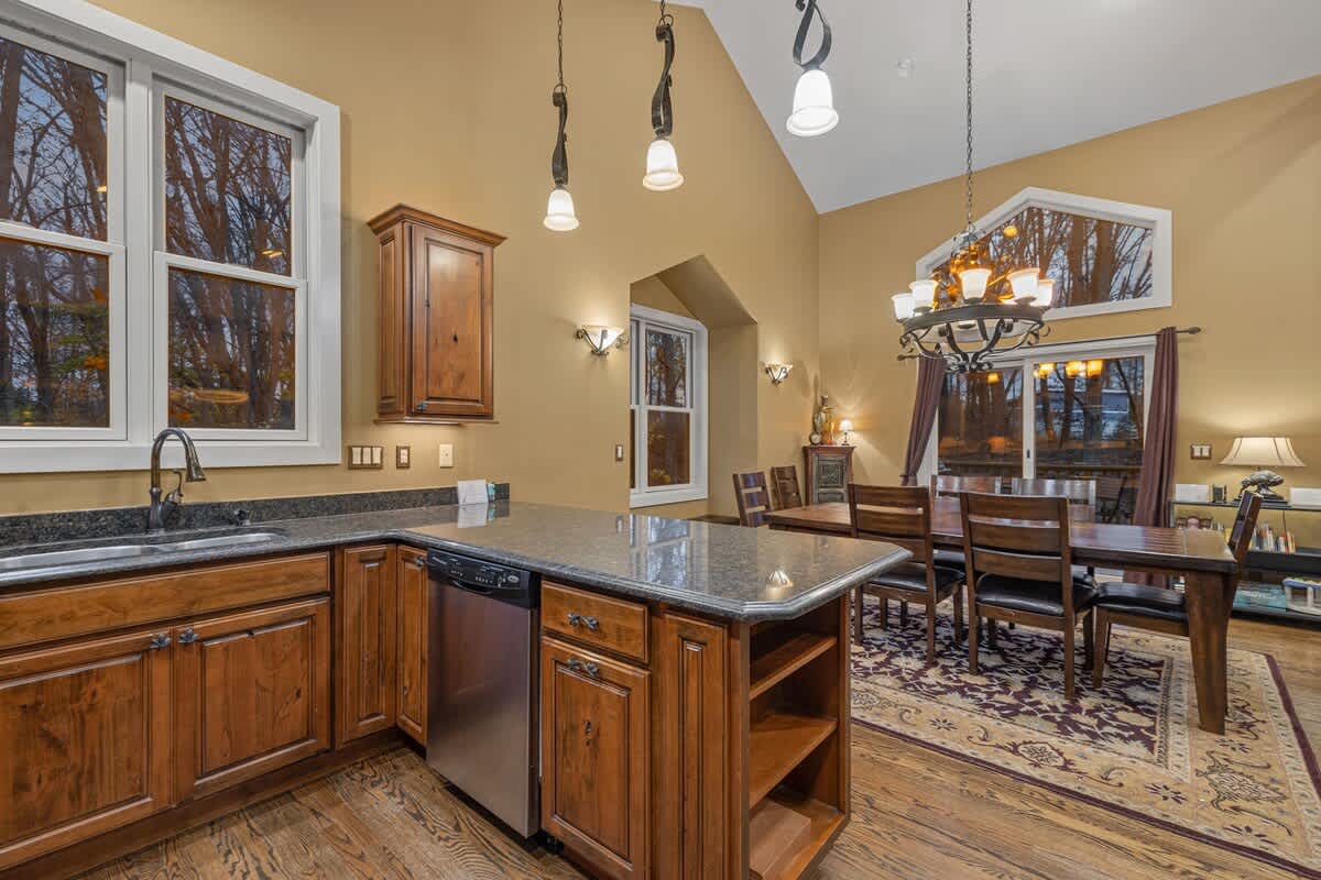View of the kitchen island with a dishwasher and sink, looking towards the dining area with a large wooden table and chandelier, all set against warm-toned walls and hardwood floors.