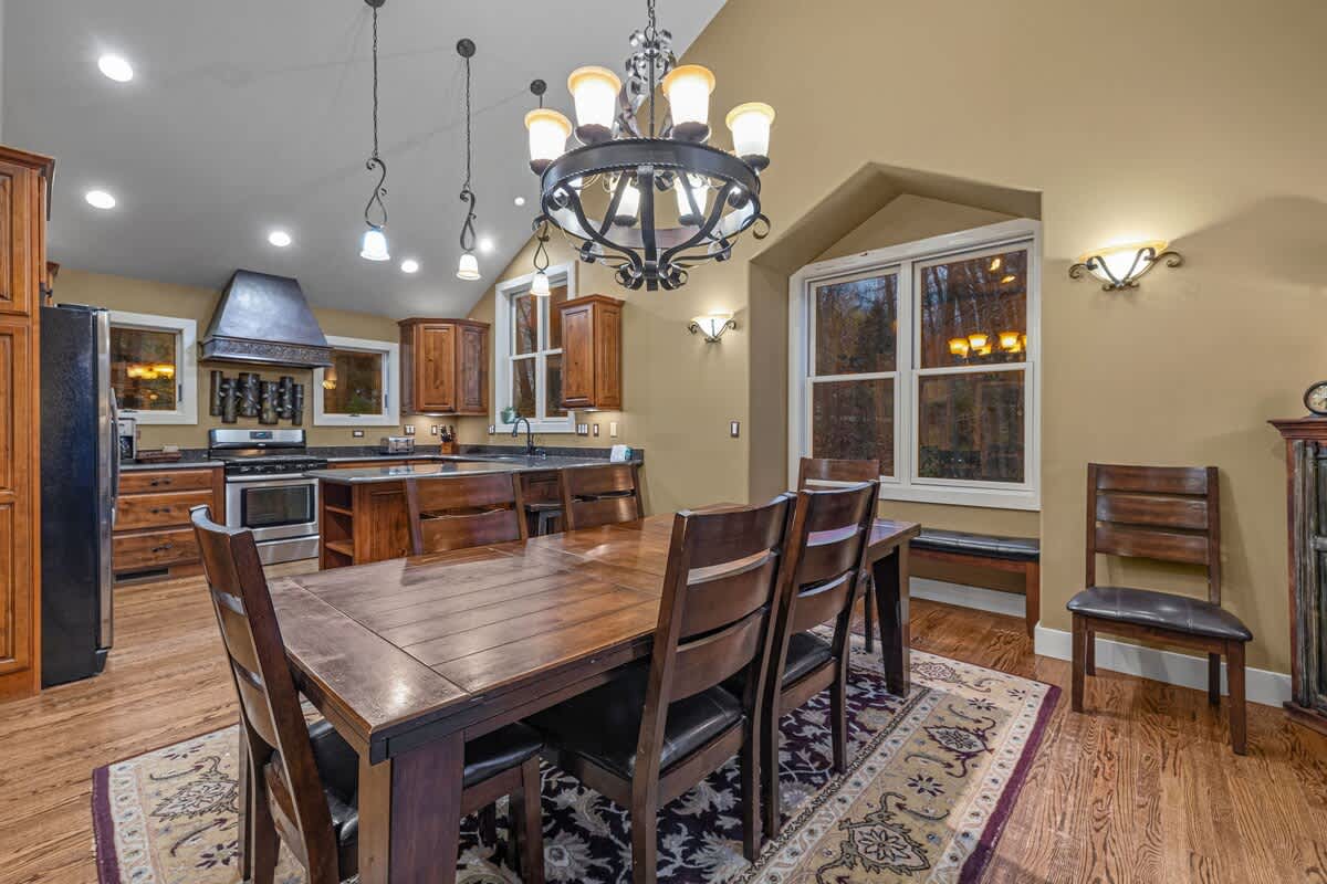An open-concept dining area with a large wooden table and chairs, flowing into a kitchen with wood cabinetry, granite countertops, and stainless steel appliances.
