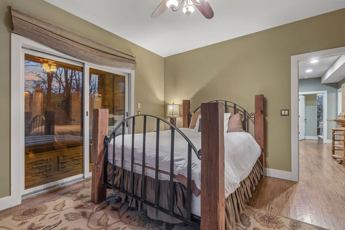 Cozy bedroom featuring a large bed with a black metal and rustic wood frame, a patterned area rug, and a sliding glass door leading to an outdoor screened porch.