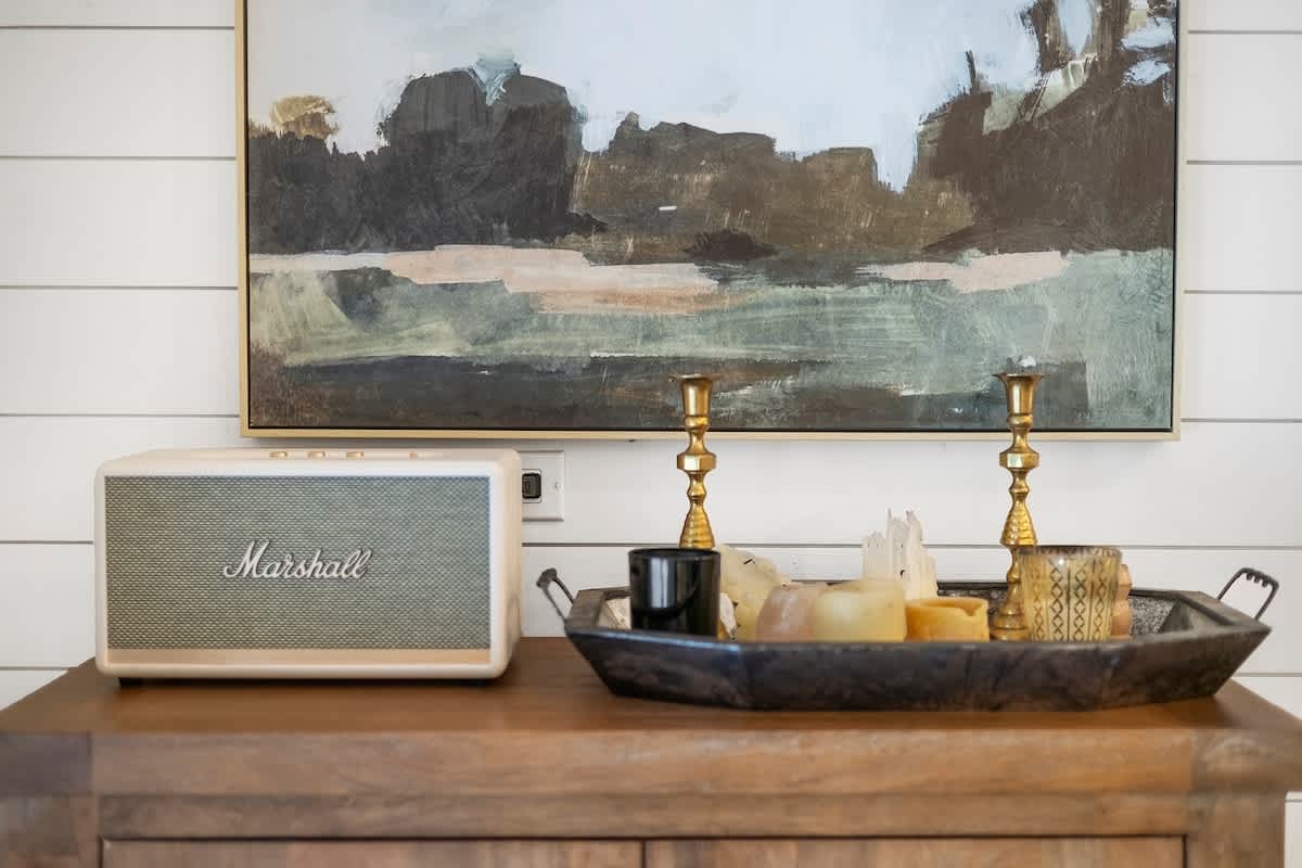 Close-up of a wooden console table in the dining area, adorned with a vintage Marshall speaker, a decorative tray with candles, and an abstract painting hanging above a white shiplap wall.