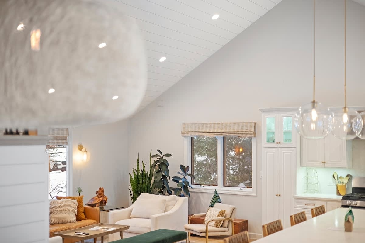 View from the dining area into the open concept living room and kitchen, showcasing the vaulted shiplap ceiling, a cozy seating arrangement, and the kitchen island with pendant lights.
