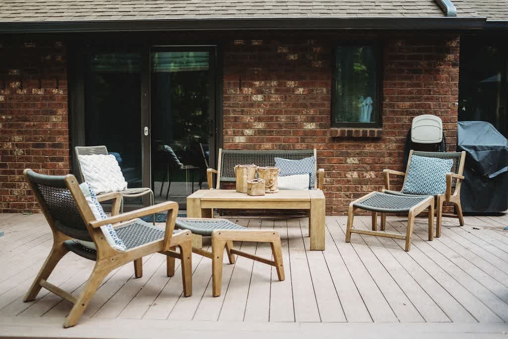 Spacious wooden deck with a modern outdoor seating arrangement, including chairs, a bench, and a coffee table, set against the brick exterior of the house.