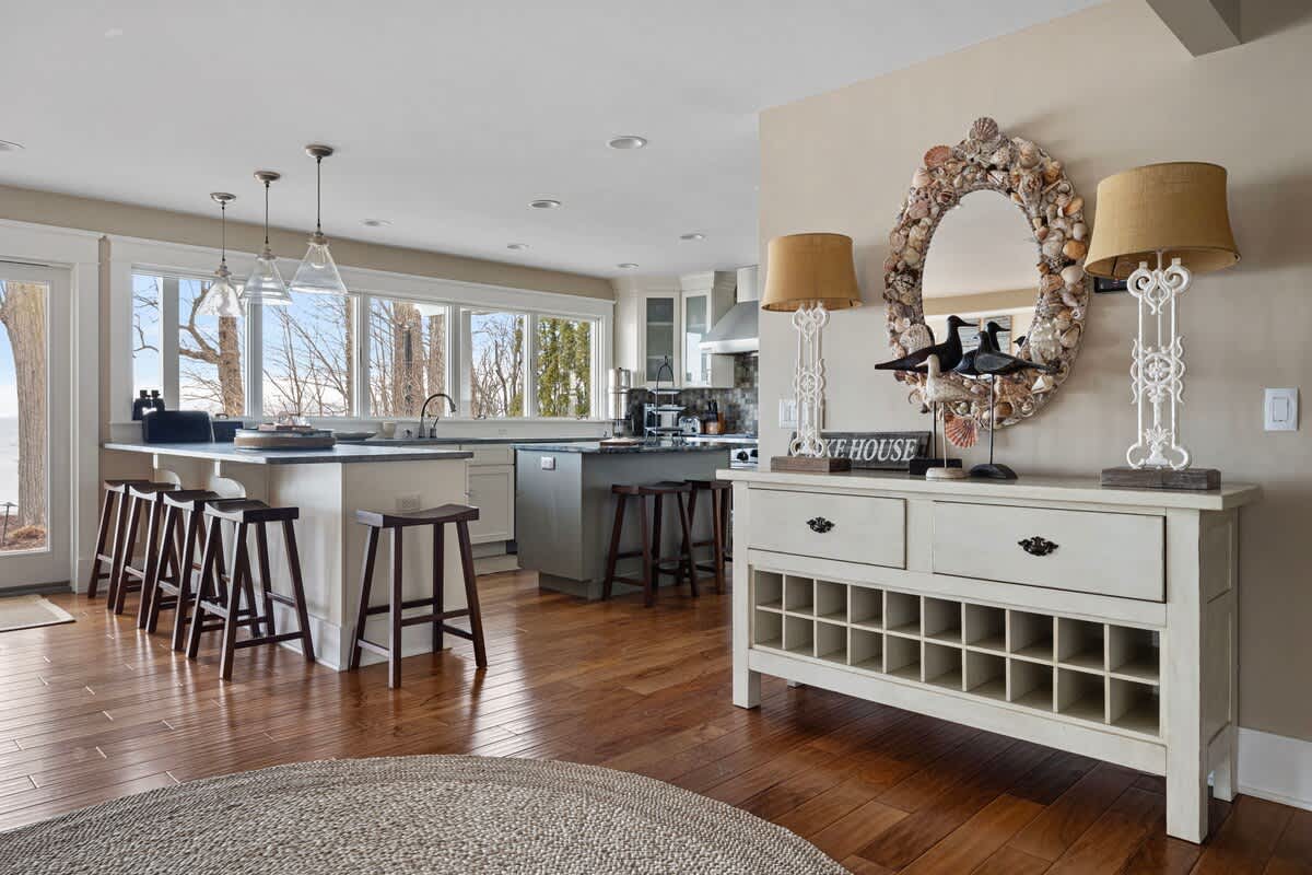 Modern open-concept kitchen with a large island and bar stools, stainless steel appliances, and ample counter space, flowing into a living area with a decorative shell mirror.