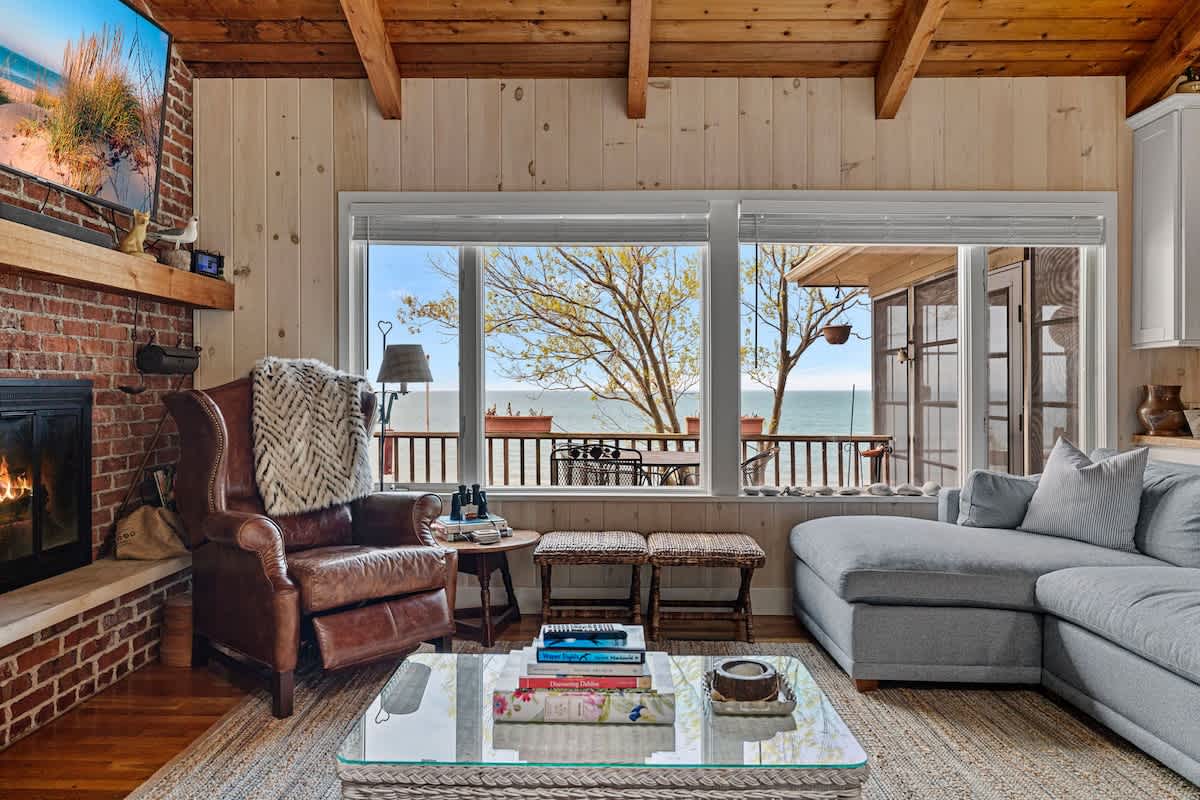 Inviting living room with a brick fireplace, a comfortable leather armchair, and a light blue sectional sofa, offering views of the lake through large windows.