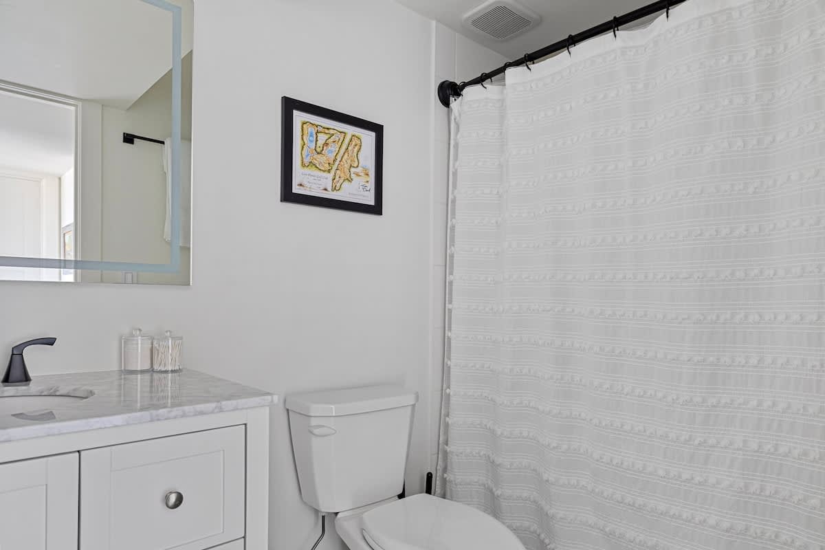 A modern bathroom with a white vanity, marble countertop, black faucet, and a white shower curtain with textured stripes, complemented by a framed map on the wall.