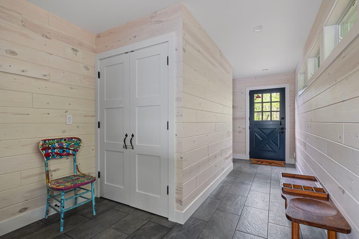 Entryway with light wood-paneled walls, dark tiled floor, a small wooden bench, and a dark blue Dutch door, leading into the home.