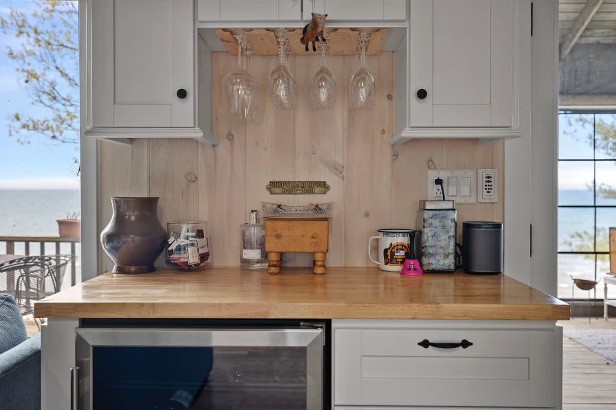 Cozy wet bar area featuring a wooden countertop, a built-in beverage cooler, and overhead wine glass storage. The space is decorated with nautical-themed items and offers a glimpse of the lake through a window.