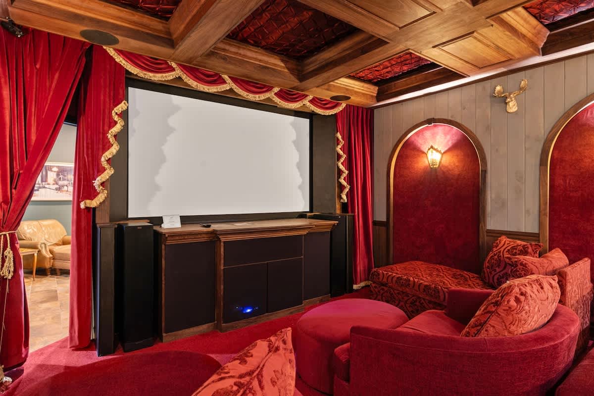 A luxurious home theater with red velvet curtains and seating, a large projection screen, and a coffered wooden ceiling, creating a classic cinematic ambiance.