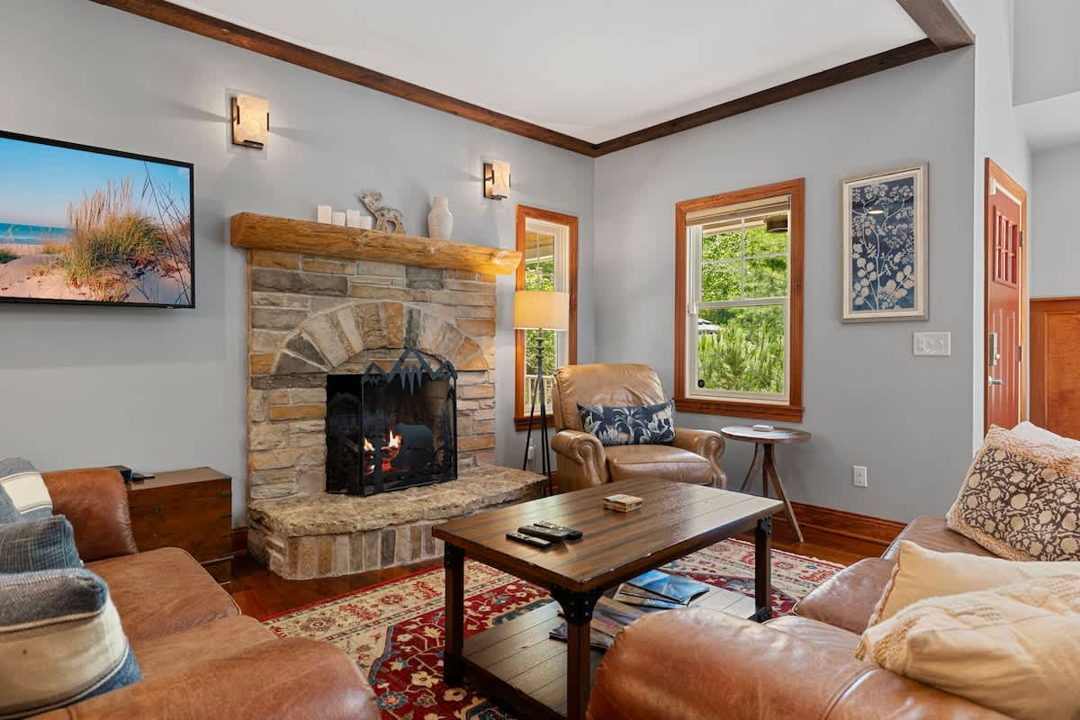 A warm living room with light gray walls, a large stone fireplace, and comfortable brown leather sofas and armchairs arranged around a wooden coffee table.