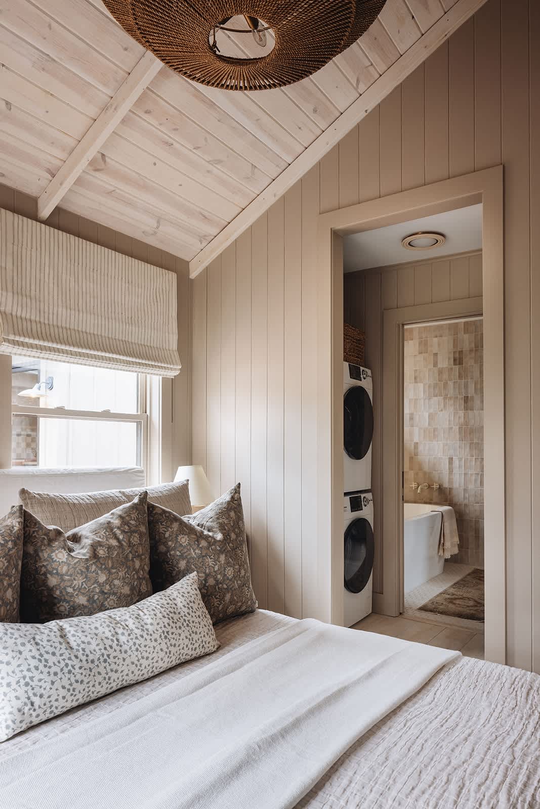 Bedroom view looking into an open doorway revealing a compact laundry area with stacked washer and dryer units, and a glimpse of a tiled bathroom beyond.