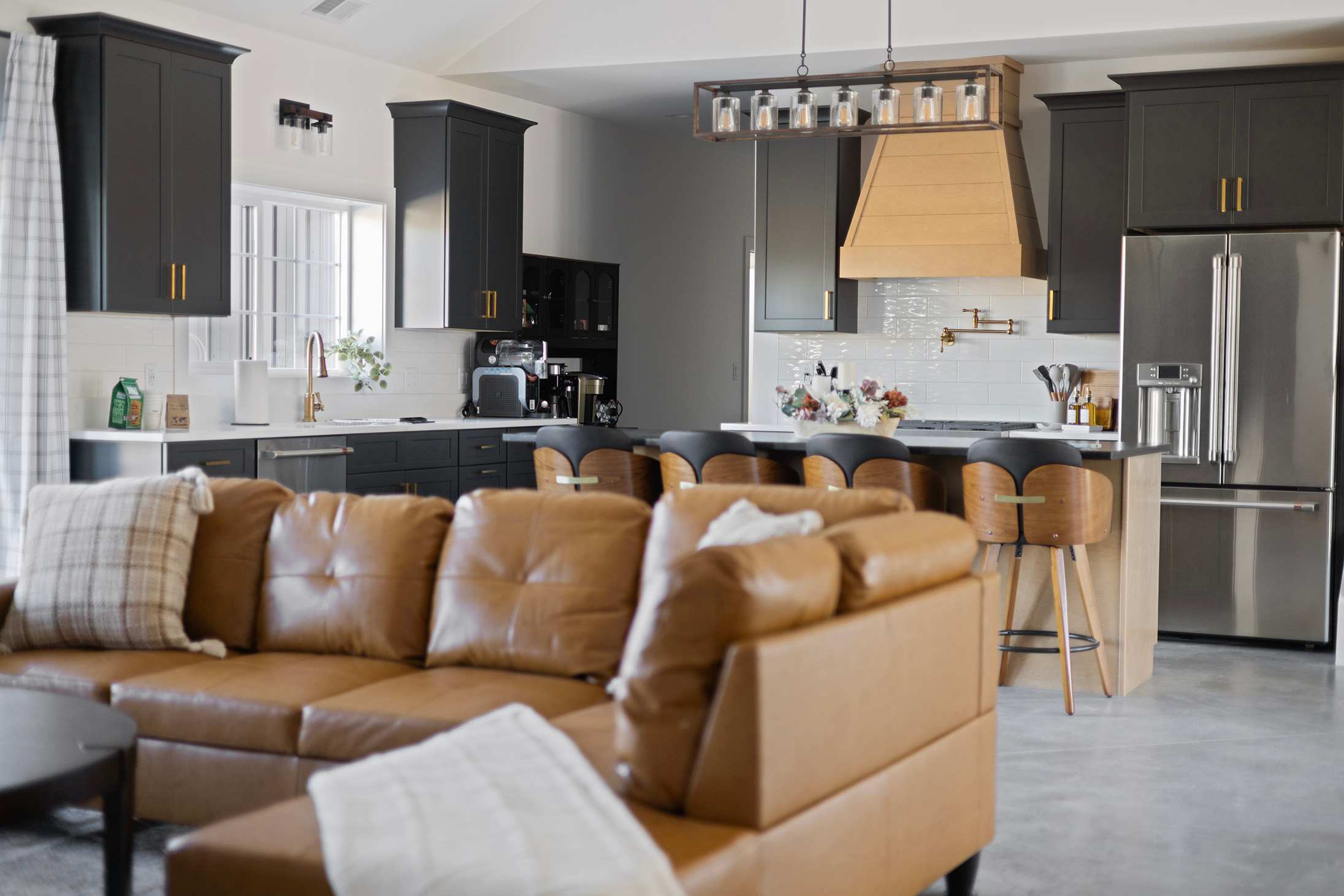 View of the modern kitchen from the living area, showcasing dark gray shaker-style cabinets, white subway tile backsplash, stainless steel appliances, and a large island with bar stools.