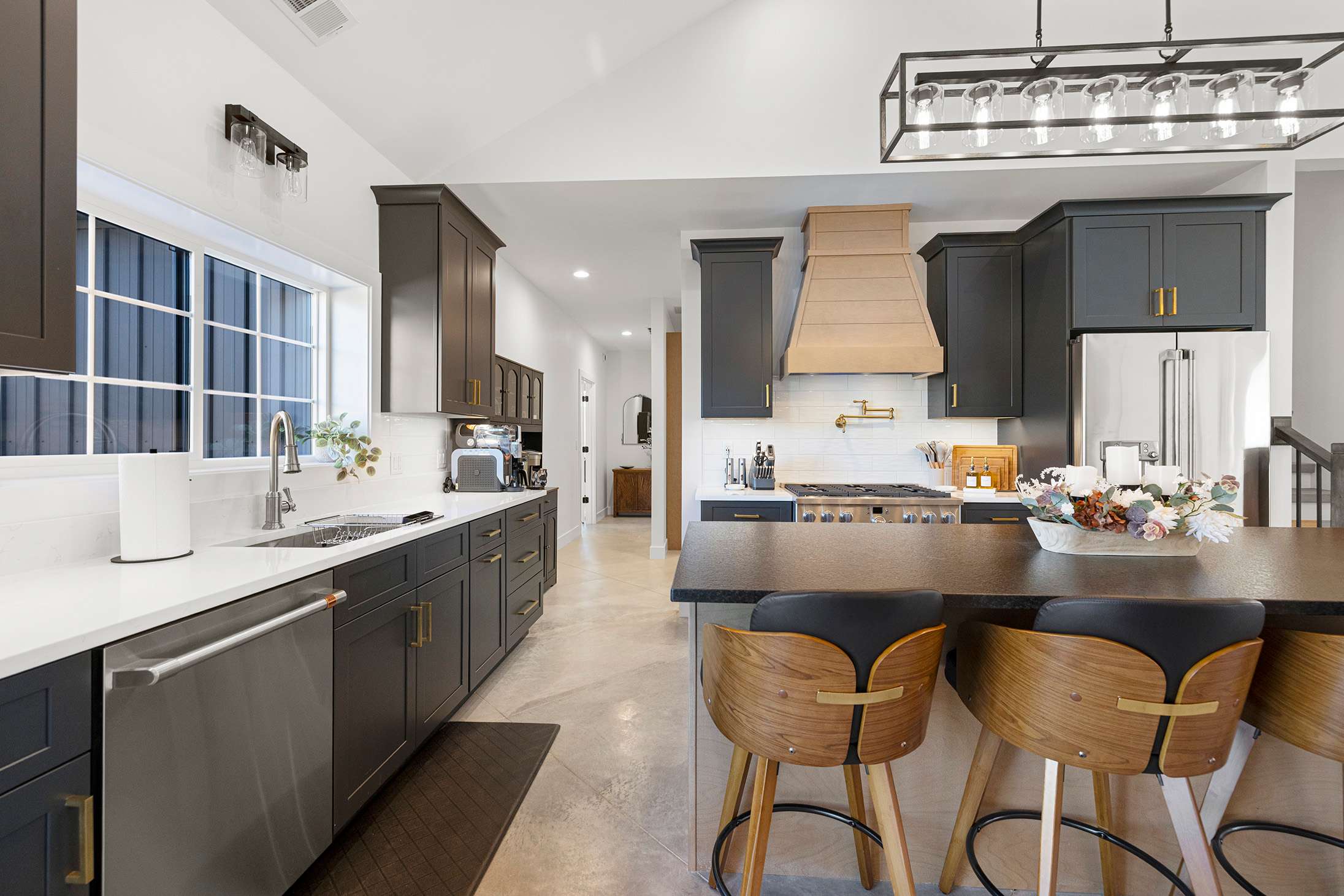 Detailed view of the kitchen counter area with a stainless steel sink, dishwasher, white quartz countertops, and dark gray shaker-style cabinets, illuminated by a window.