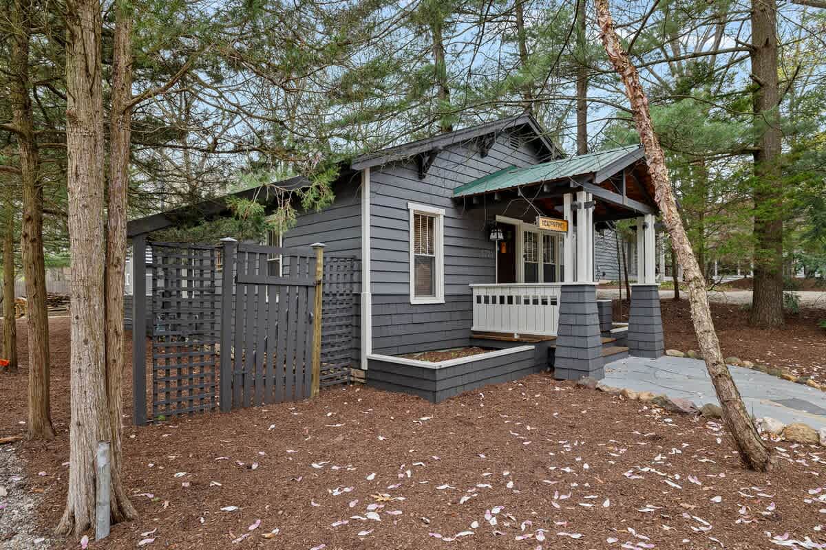 The front exterior of a dark gray house with white trim and a green roof, featuring a welcoming porch with white railings and a decorative dark gray lattice fence.