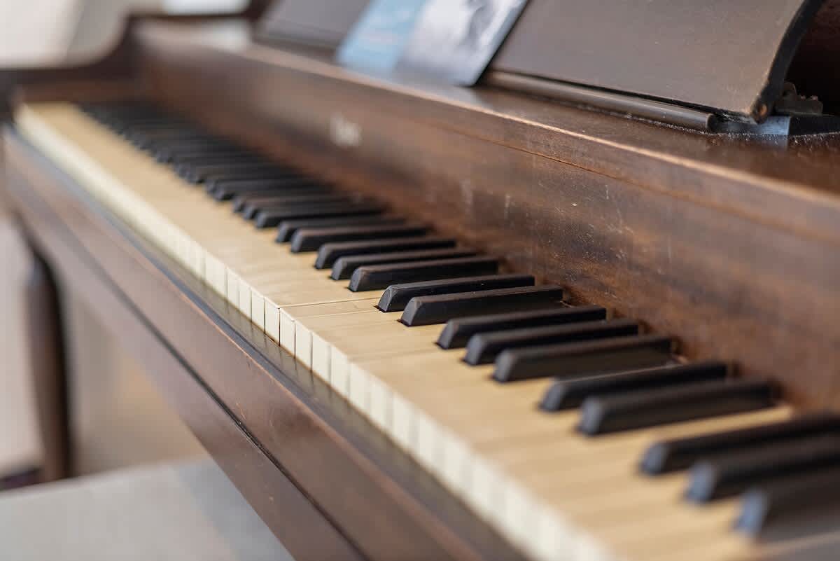 Close-up view of a vintage dark wood piano keyboard with white and black keys, showing some wear on the wood finish.