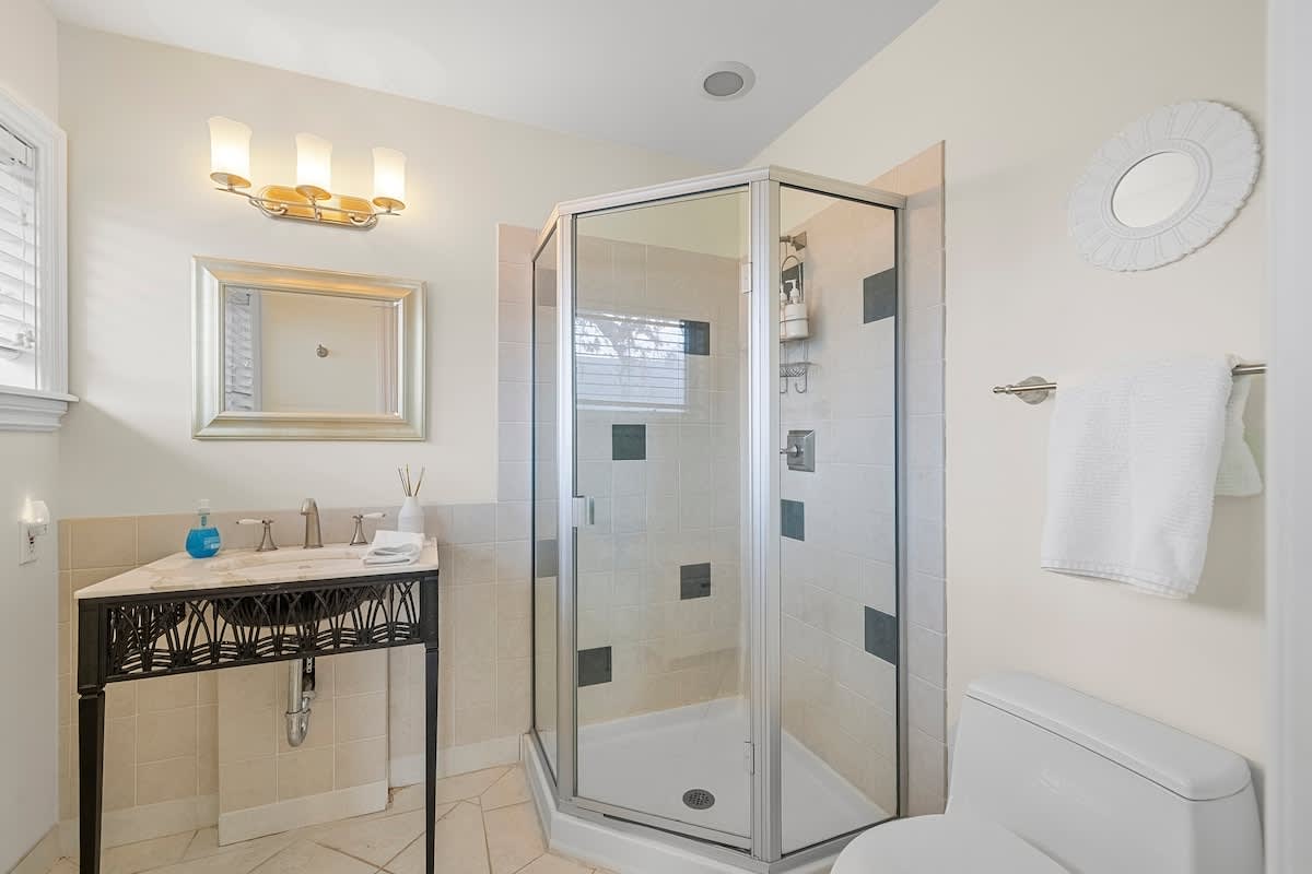 Compact bathroom featuring a corner glass-enclosed shower, a pedestal-style vanity with a sink, and a toilet. The room has tiled flooring and light-colored walls.
