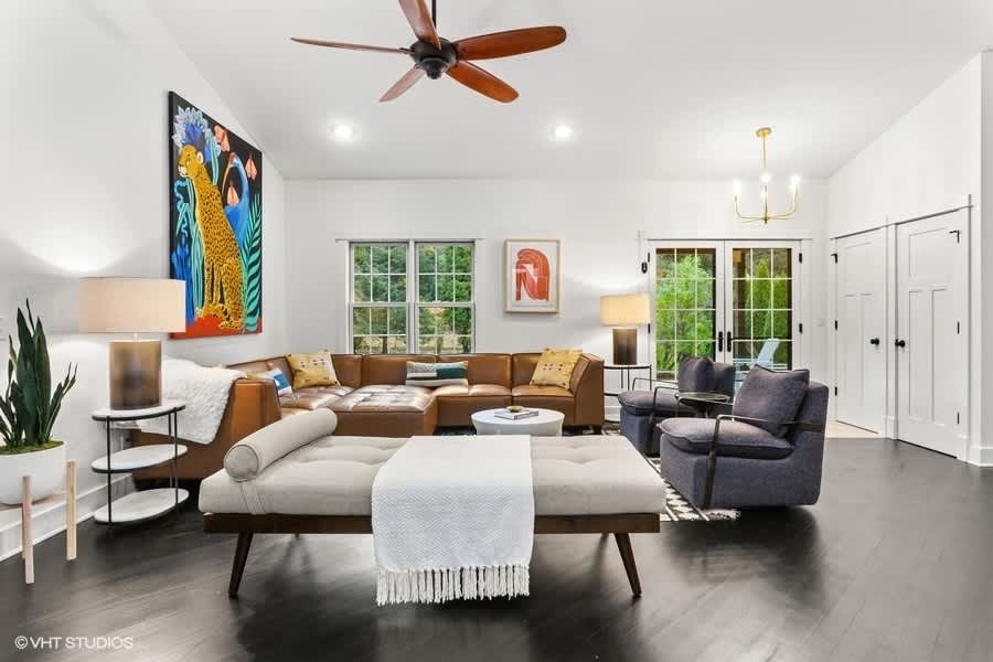 Bright living room with dark hardwood floors, a large brown leather sectional, and a vibrant cheetah painting on the white wall. A modern ceiling fan and recessed lighting illuminate the space.