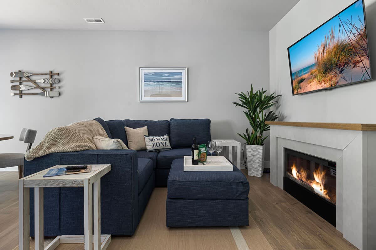 Cozy living room featuring a large blue sectional sofa with decorative pillows, a modern fireplace with a light wood mantel, and a wall-mounted flat-screen TV.