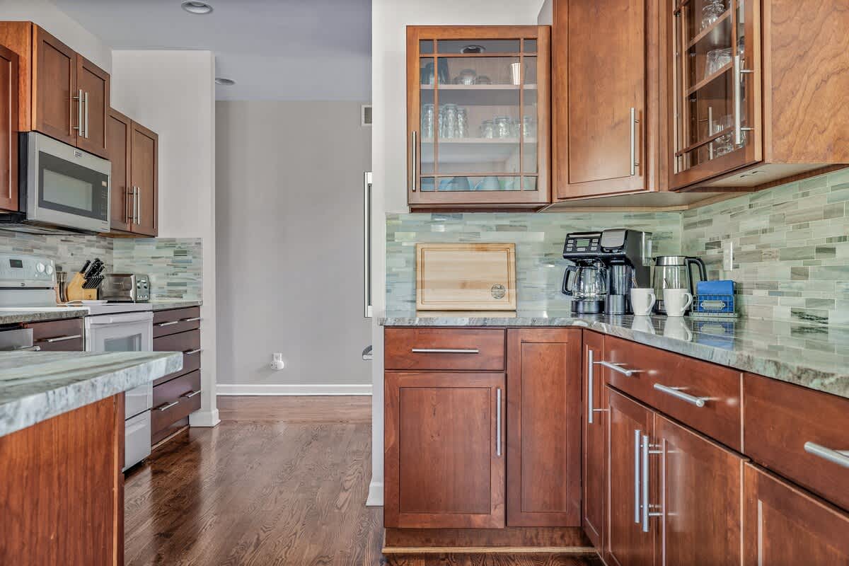 A well-equipped kitchen corner featuring dark wood cabinetry, light-colored granite countertops, a stylish tiled backsplash, and various small appliances like a coffee maker and microwave.