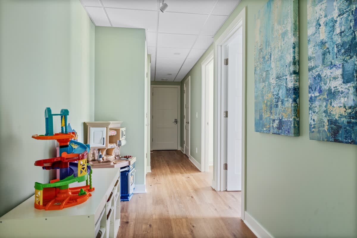 Bright hallway with light green walls, featuring children's toys on a low white cabinet and two abstract blue and white artworks, leading to other rooms.