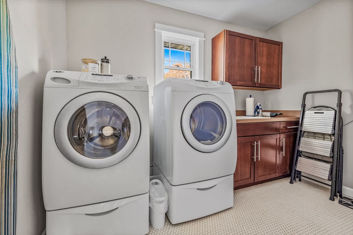 Functional laundry room equipped with a front-loading washer and dryer, dark wood upper and lower cabinets with a utility sink, and a small window for natural light.