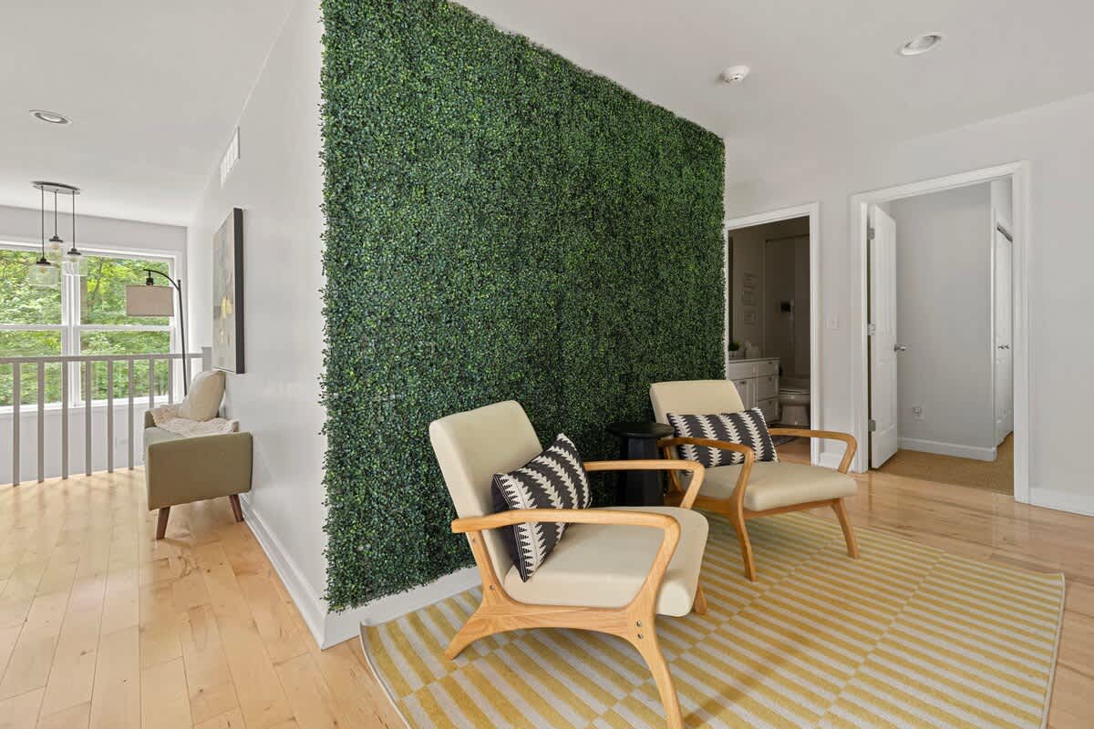 A unique upstairs common area with light hardwood floors, featuring a striking faux green wall, two mid-century modern armchairs with geometric pillows, and a yellow and white striped rug.