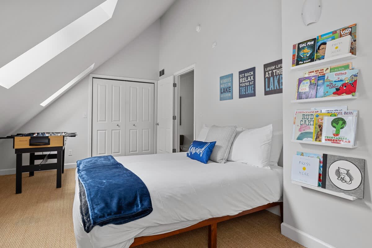 A playful children's bedroom with a single bed, a foosball table, and shelves displaying children's books. The room features a sloped ceiling and a closet, on a natural fiber rug.