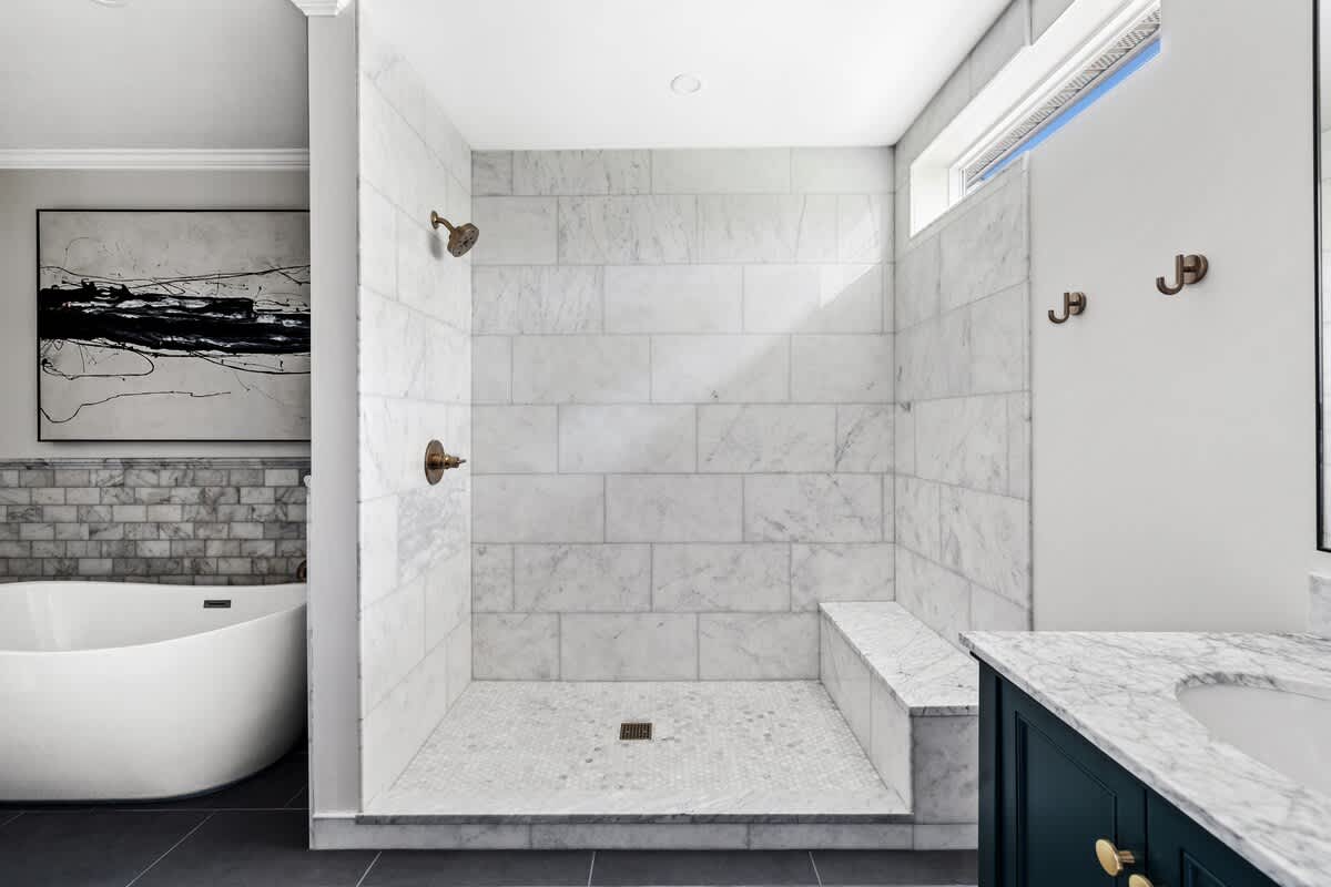 Modern bathroom featuring a spacious walk-in shower with white marble subway tiles, a built-in bench, and bronze fixtures, adjacent to a sleek white freestanding bathtub.