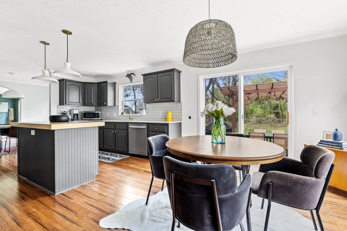 Spacious open-concept kitchen featuring dark gray shaker cabinets, light countertops, a central island, and a dining area with a round wooden table, all with views of the backyard through a large sliding door.