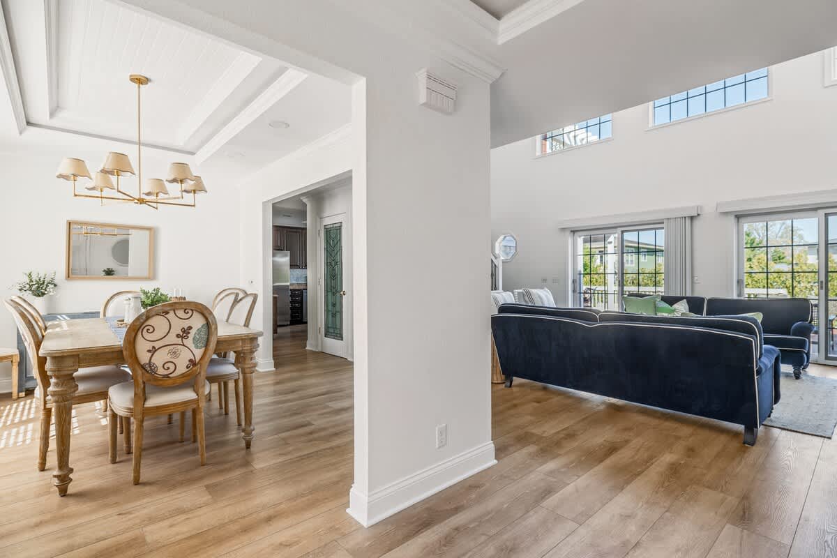 Expansive open-concept living space with a navy blue sofa, light wood flooring, and a view into the adjacent dining room and kitchen, featuring large sliding glass doors leading to an outdoor area.