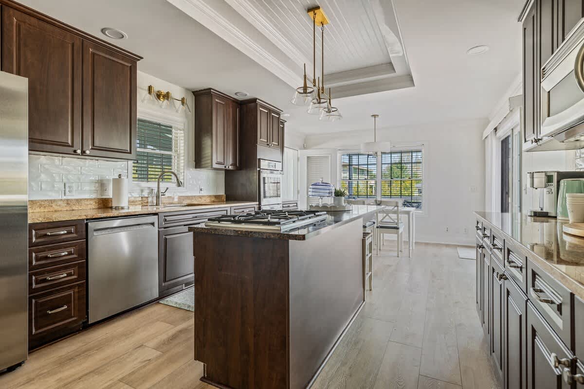 Spacious kitchen with dark wood cabinets, granite countertops, and a central island, extending to a bright breakfast nook with a white table and chairs, and sliding glass doors leading to an outdoor area.