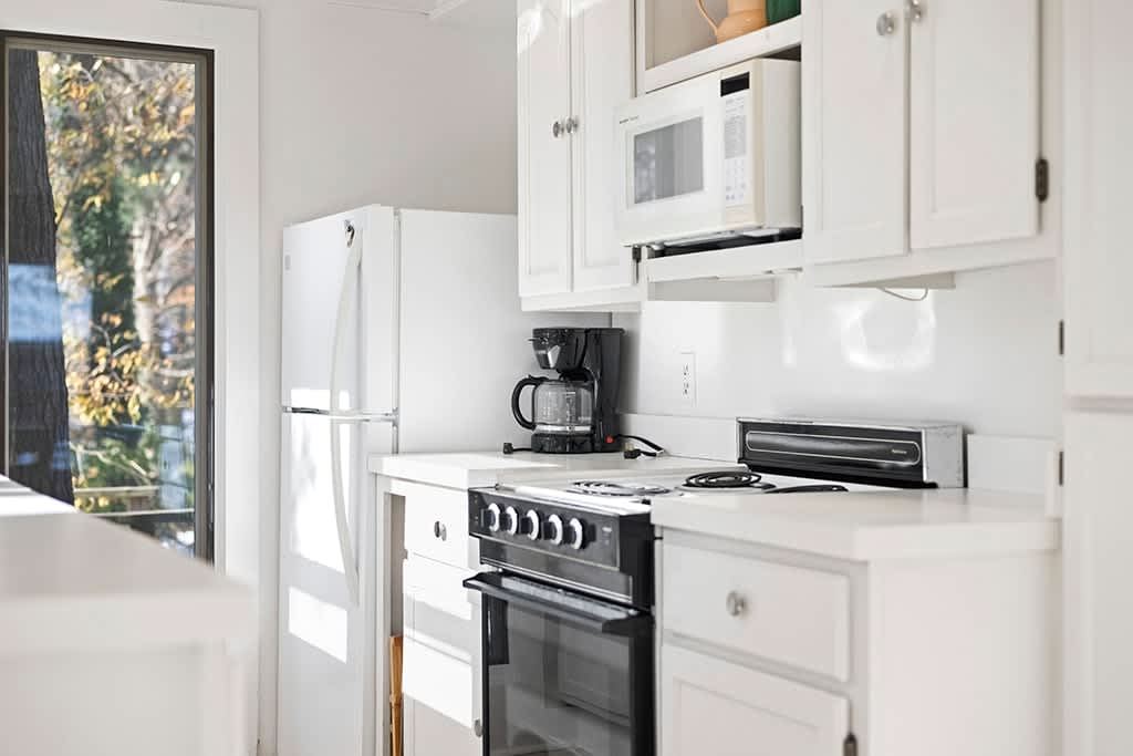 A section of the kitchen showcases white cabinetry, a white refrigerator, a black coffee maker, a black electric stove with an oven, and a white microwave mounted above the counter.