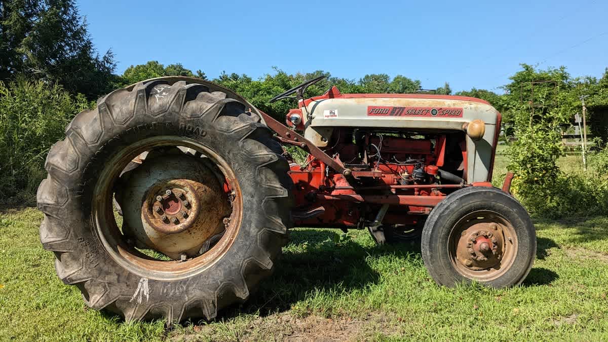 A vintage red and white Ford tractor with large rear tires is parked on a grassy area under a clear blue sky, showcasing its classic farm machinery design.