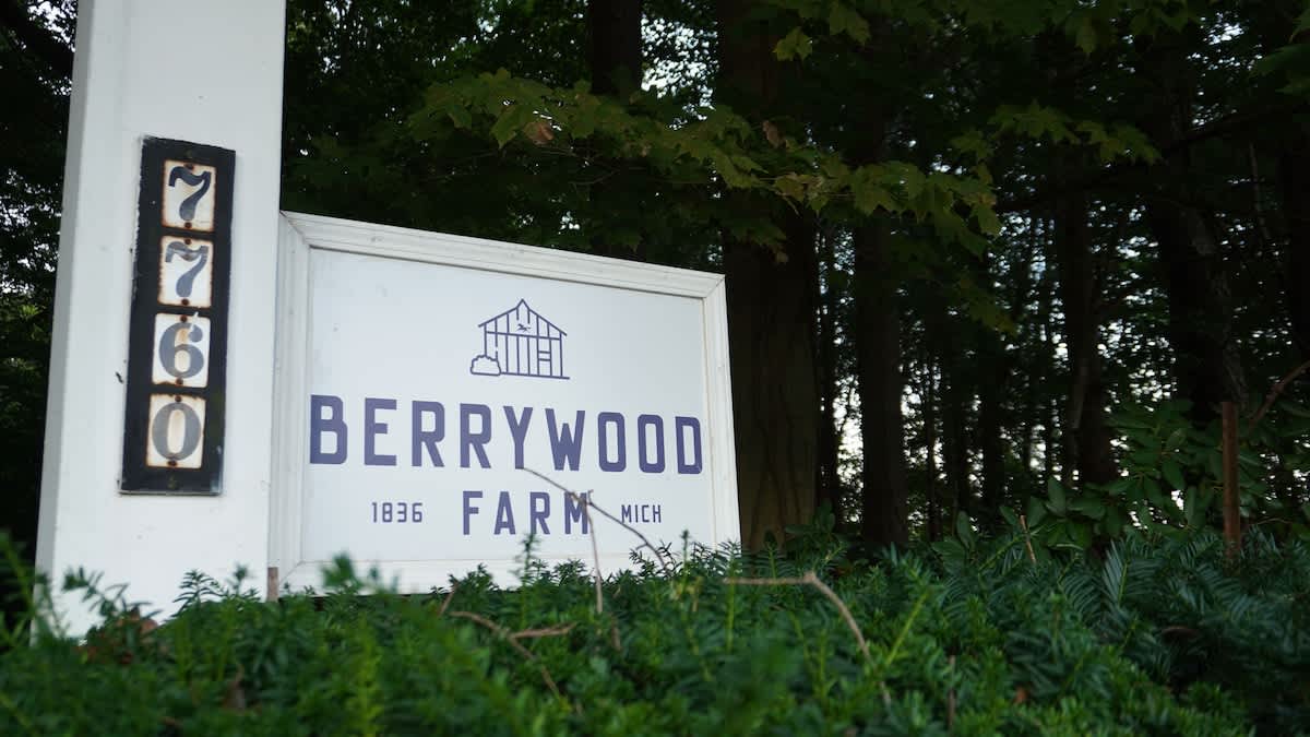 A white wooden sign with the address "7760" and "BERRYWOOD FARM 1836 MICH" in blue lettering, partially obscured by green foliage, marks the property entrance.