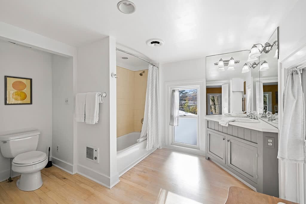 Another angle of the white-walled bathroom, highlighting the toilet area and the bathtub/shower combo with a yellow tiled surround and a striped shower curtain.