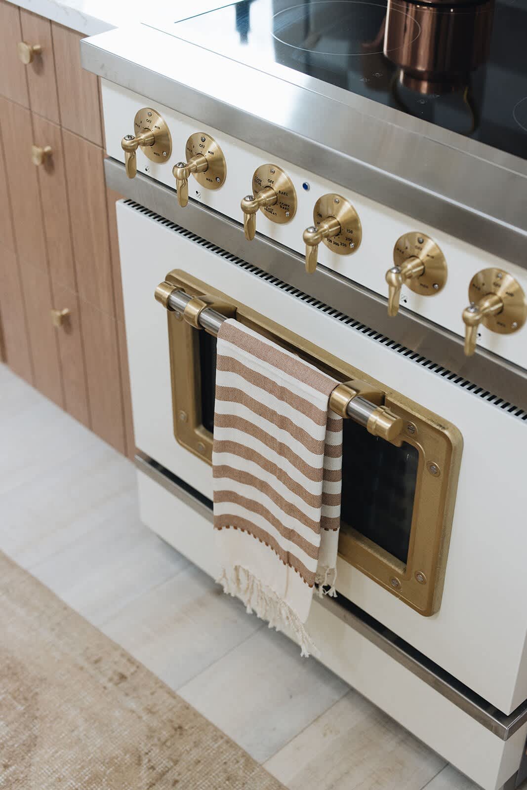 A detailed shot of the white and brass vintage-style oven, highlighting its ornate brass knobs and handle, with a striped towel hanging from the handle.