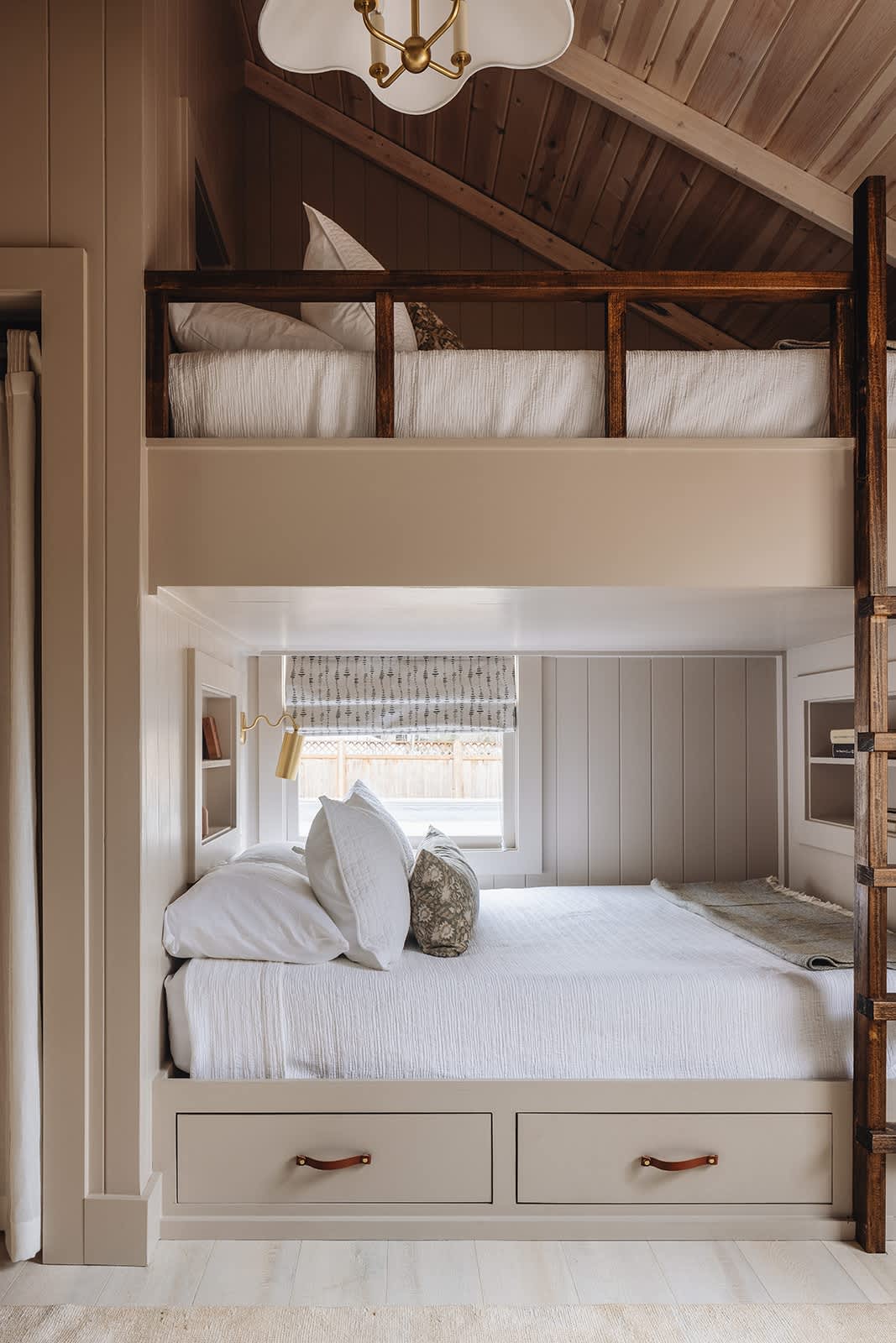 Close-up of the built-in bunk beds in a bedroom, showing the lower bunk with storage drawers and a small built-in shelf, and the upper bunk with a dark wood railing.
